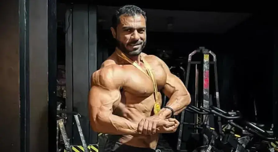 A victorious Pakistani bodybuilder holding a gold medal and draped in the national flag, standing confidently on an international competition stage, symbolizing national pride and athletic excellence.